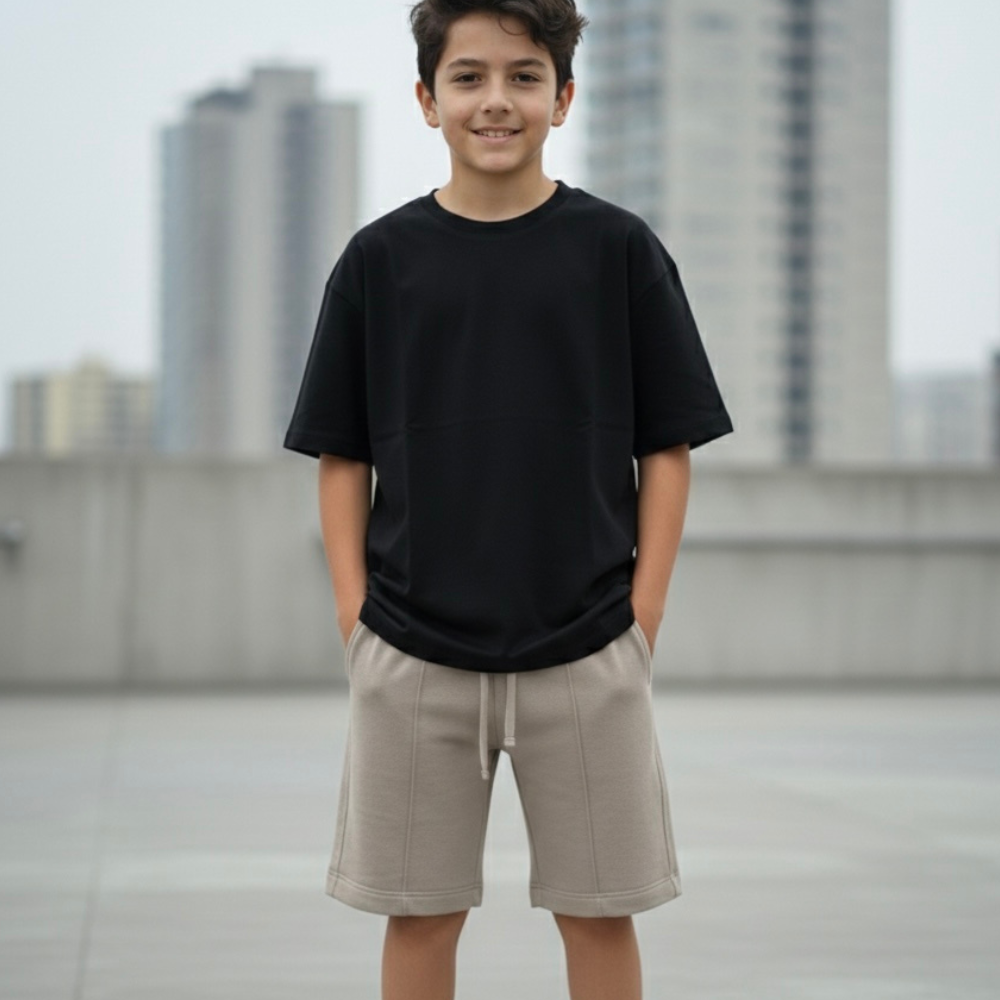 Niño con short arena de cordón frontal y polo negro, con las manos en los bolsillos.