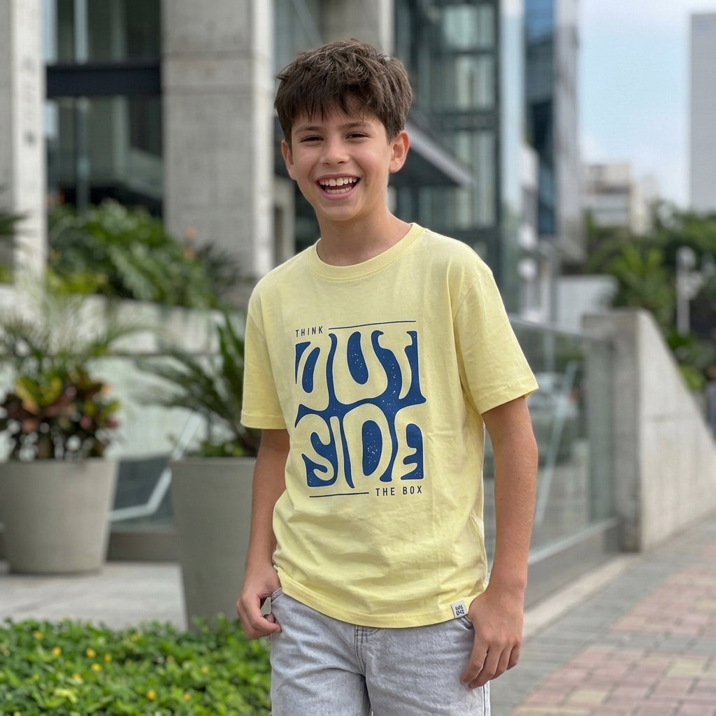 Niño sonriendo con polo amarillo Think Outside de manga corta y estampado azul de ANG Kidz.